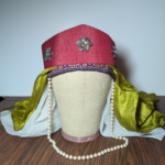 Front view of a canvas mannequin head wearing a red hat over a green scarf and a white veil
