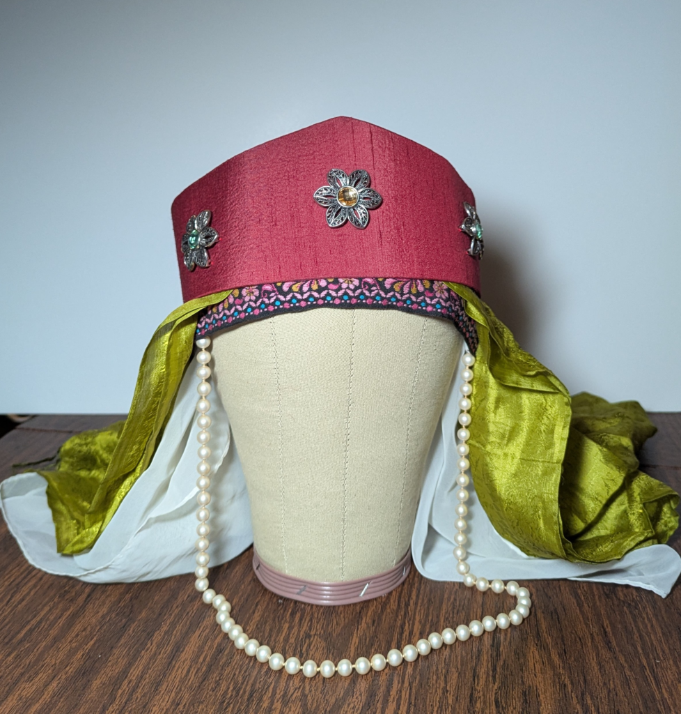 Front view of a canvas mannequin head wearing a red hat over a green scarf and a white veil
